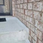 A pristine, freshly tooled exterior caulking joint sealing a concrete porch landing pad against a red clay brick masonry wall.